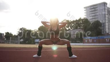 一个肌肉发达的妇女在户外体育场锻炼的肖像。一个穿着比基尼的健身女孩一边做仰卧<strong>起坐</strong>